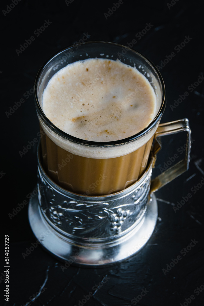 Aromatic cappuccino coffee in a glass cup with a vintage coaster on a dark concrete background with copy space. Aromatic cappuccino coffee in a glass cup with a vintage coaster on a dark concrete background with copy space.