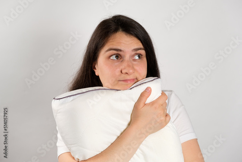 A woman hugs a pillow and looks away on a white background  copying space for text