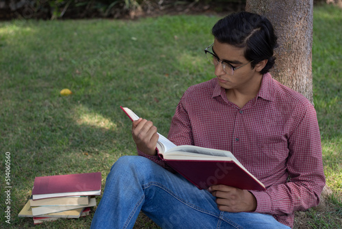 attractive and intelligent young man reads books sitting in the grass, amidst the silence and peace of nature.