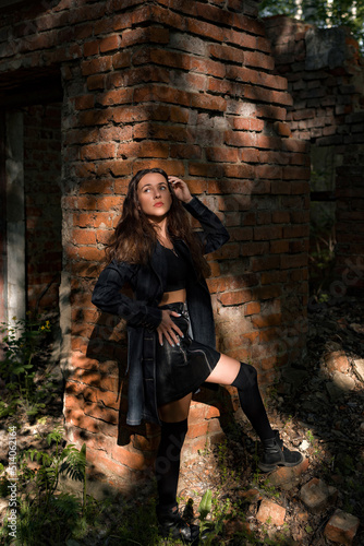 beautiful woman in black stockings and a black skirt in the woods near a brick wall