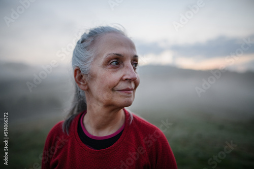 Cheerful senior woman in nature on early morning with fog and mountains in background.
