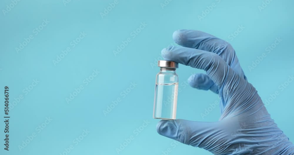 Hand in blue gloves hold the vial with vaccine or drug on blue background. Hand in blue gloves hold the vial with vaccine or drug on blue background.