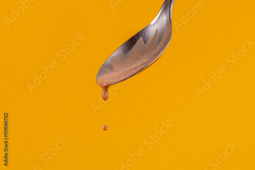 Colher derrubando sorvete de chocolate e gota flutuando sobre fundo amarelo photo