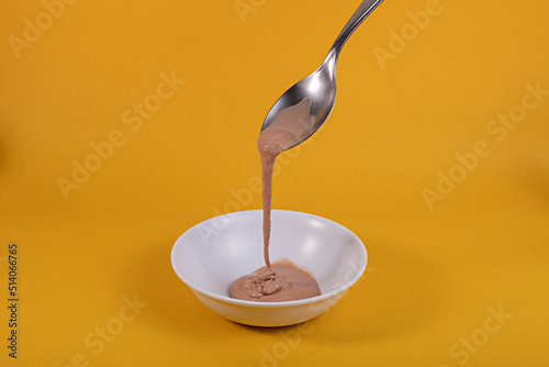 Colher derrubando sorvete de chocolate derretido sobre uma tijela branca com fundo amarelo