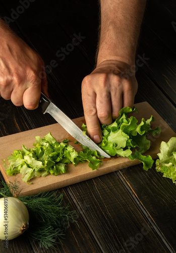 The chef cuts fresh Lettuce leaves on a cutting board for a vitamin salad. Diet menu for breakfast