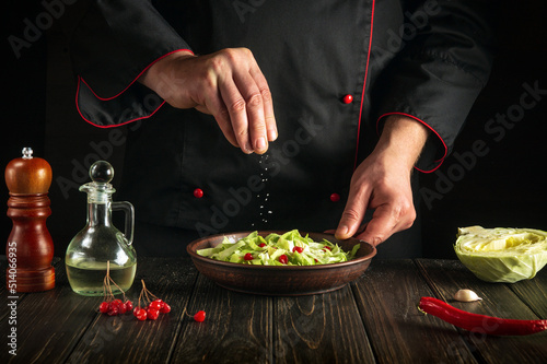 Fototapeta Naklejka Na Ścianę i Meble -  Chef salts a fresh vegetable salad. Menu idea for a hotel. Grand cuisine