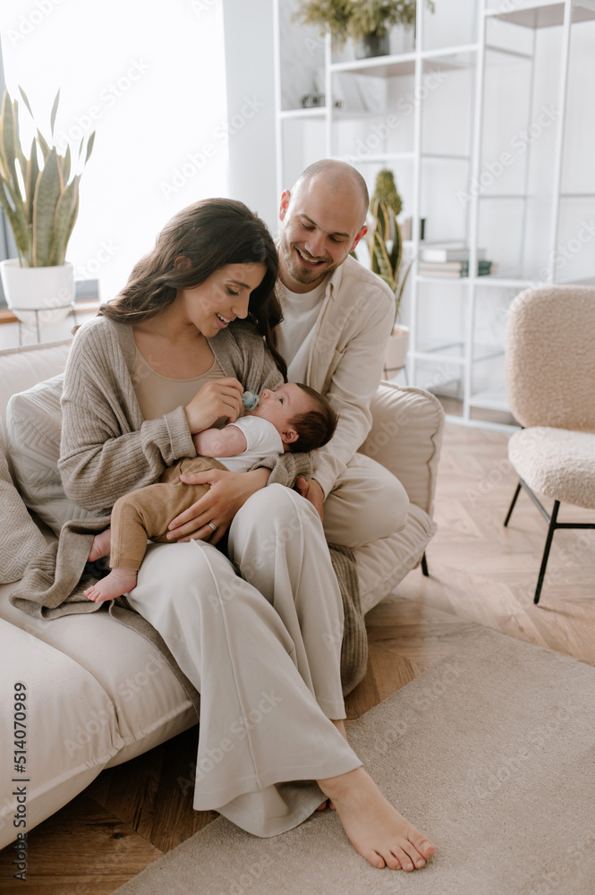 Mother and father holding their infant in minimalistic interior kissing small cute hand family 