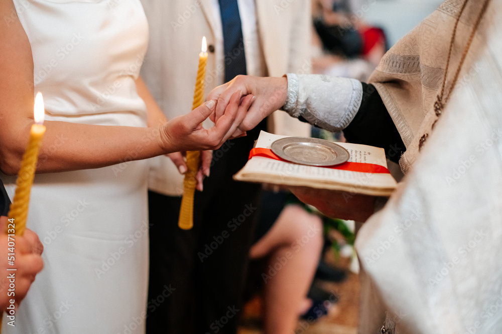 Obraz premium A couple holding hands during a wedding ceremony, with a priest in the background. A touching moment of commitment and love.