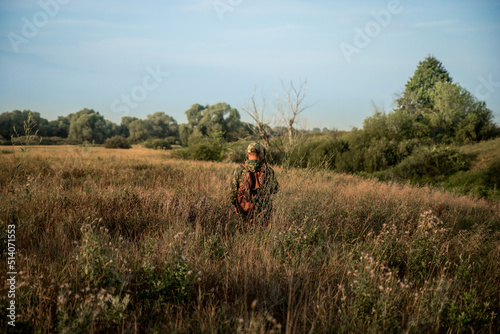 Hunter in camouflage with shotgun creeping through tall reed grass and bushes during hunting season 