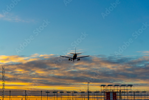 The silhouette of a passenger plane coming in for landing against the backdrop of the sunset sky.