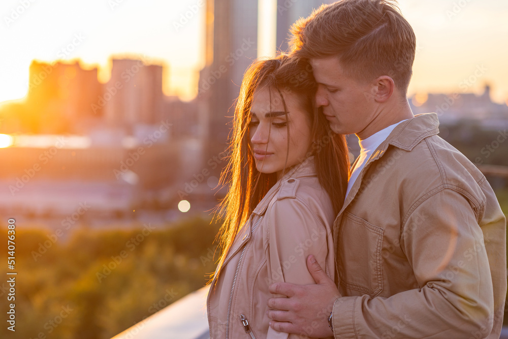 Beautiful happy young loving couple on a surprise date on a Saint Valentine's Day. Romantic date on the rooftop, summertime. Young man and beautiful girl. Newlyweds on honeymoon. Golden hour Beautiful happy young loving couple on a surprise date on a Saint Valentine's Day. Romantic date on the rooftop, summertime. Young man and beautiful girl. Newlyweds on honeymoon. Golden hour