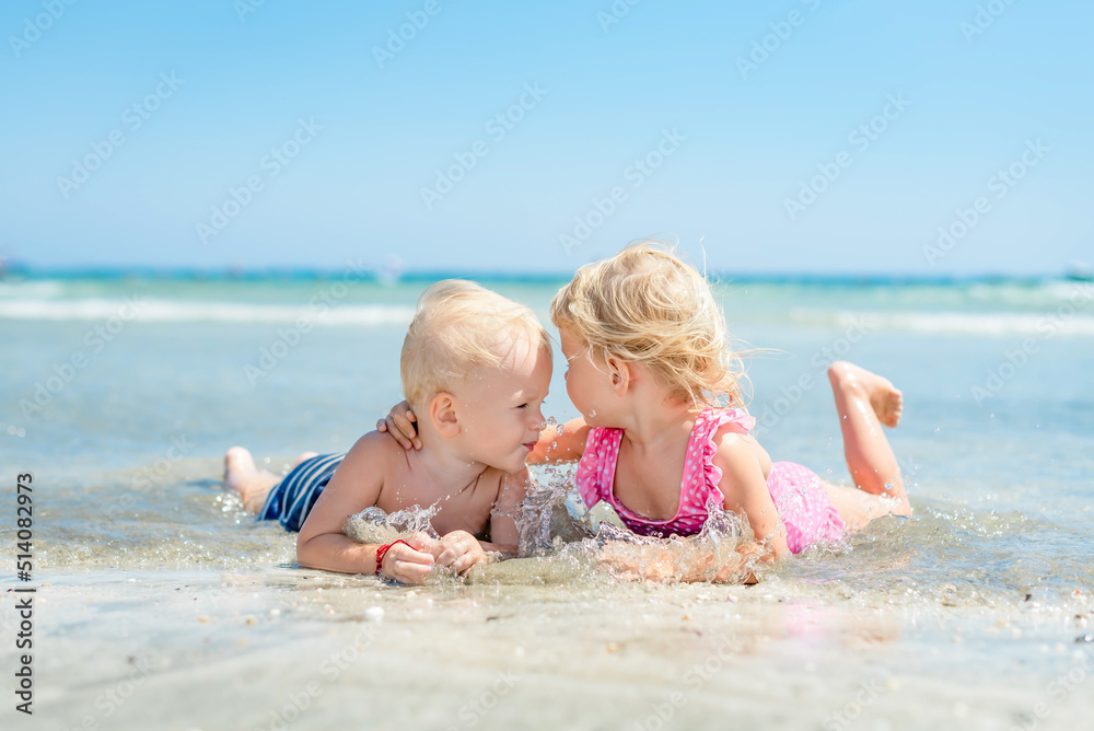 little girl hugging boy lying on beach in sea in ocean