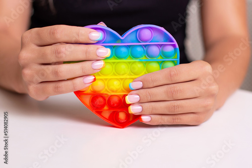 Beautiful female hands with colourful manicure nails holding toy, pop it 