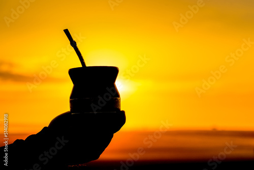 Fotografie Silhouette of a hand holding a yerba mate drink at golden sunset