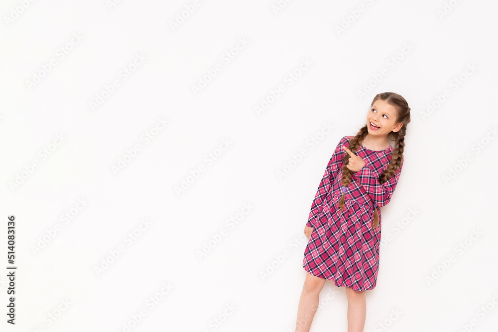 A little girl in a pink plaid dress looks at your advertisement on a white isolated background. Copy space.