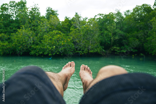 Obraz na plátně Legs point of view of alone male who sit and sleep over the water surround mangrove forest during holiday in Southeast Asia