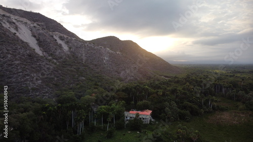 paisaje de montañas escondiendo el sol en un amanecer de montaña junto a un verde grandioso de un bosque de alrededory una casa grande en medio del bosque