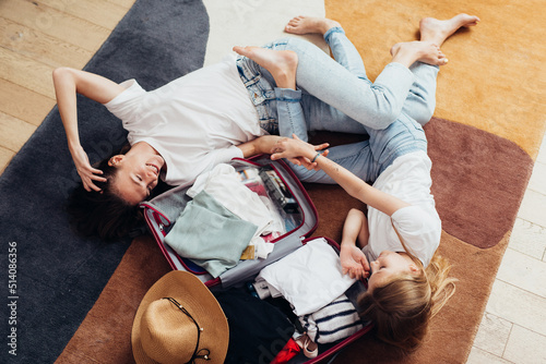 Mother and daughter dreaming of a travel, lying on the floor, packing a suitcase photo