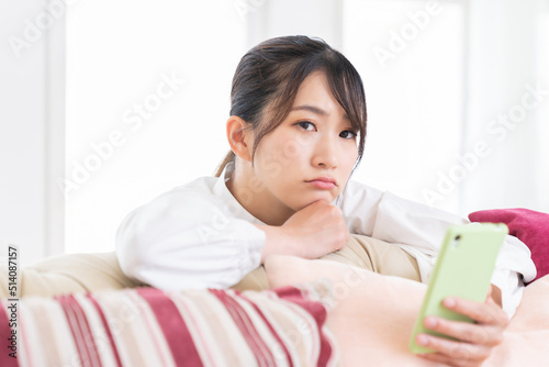 部屋でスマホを見る女性 考える