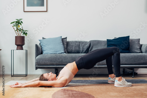 Fit woman exercises at home doing gluteal bridge photo