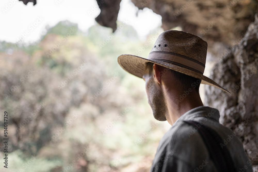 An unrecognizable young man wearing a hat is looking down from the heights of a cave