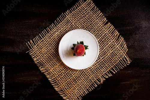 Conceptual photo of a strawberry in a white plate on a jute backing