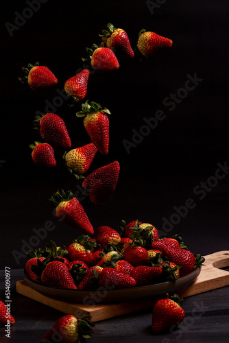 Strawberries falling into a plate on a wooden board