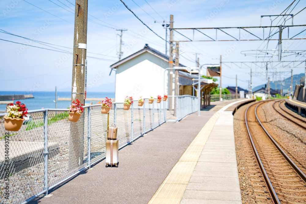 Obraz premium 初夏の旅行。カフェオレ色のスーツケースが置かれた海が見える無人駅のホーム