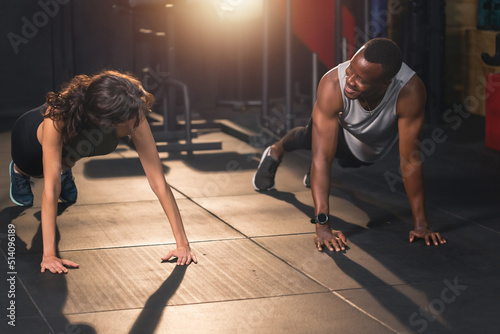 Young happy African American sportsmen and Caucasian woman making plank at the gym. Couple exercising standing in a full plank position