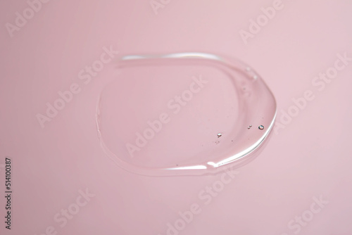 Drop of cosmetic transparent gel on a pink background. The texture of the serum, heir gel or hyaluronic booster.
