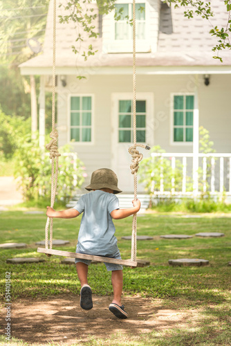boy sitting on a swing under a tree in front of his house