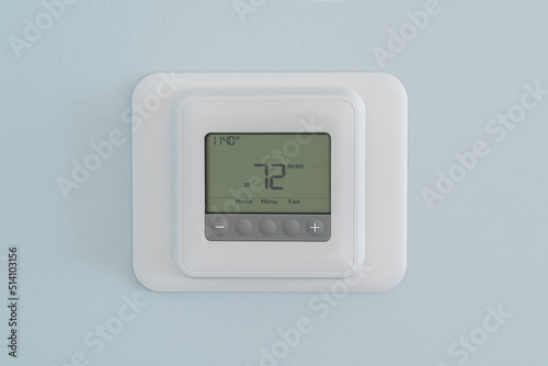 Photograph of a modern residential programmable heating and cooling thermostat set at 72 degrees mounted on a blue wall photo