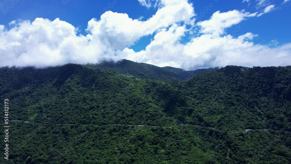 Parallel flight along highway running through dense forest-covered mountain in Eastern Taiwan on a bright day with fluffy white clouds Parallel flight along highway running through dense forest-covered mountain in Eastern Taiwan on a bright day with fluffy white clouds
