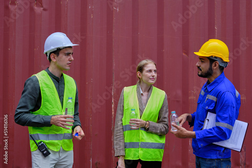 Three Caucasian workers in the freight industry in container background, take a break and relaxing from logistics work exhaust by drinking water, resting, cargo shipping transportation business.