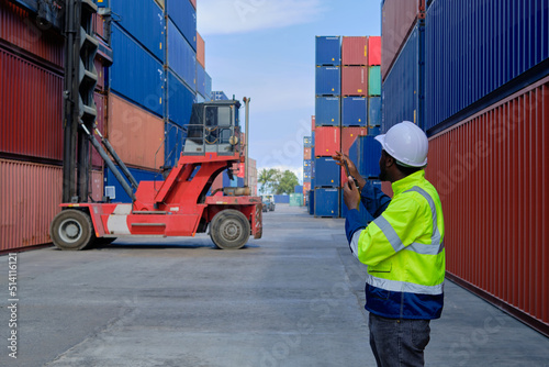 African American male worker in safety uniform and hardhat use walkie-talkie, work at logistics terminal with many stacks of containers, loading control shipping goods, cargo transportation industry.