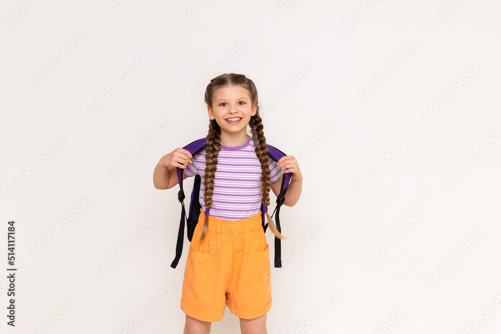 A little girl with pigtails and shorts with a school backpack on her back on a white isolated background. Preparatory summer courses for children. A little girl with pigtails and shorts with a school backpack on her back on a white isolated background. Preparatory summer courses for children.