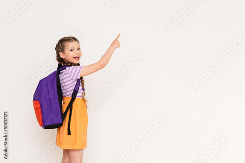 Принти на полотні A child with a satchel points with his index finger at your advertisement on a white isolated background