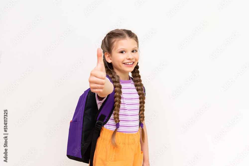 A little girl with a satchel gives a thumbs up. A beautiful child is smiling on a white isolated background. A little girl with a satchel gives a thumbs up. A beautiful child is smiling on a white isolated background.