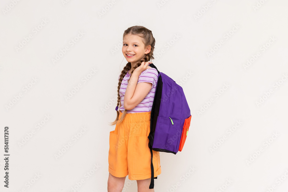 A little girl with pigtails and shorts with a school backpack on her back on a white isolated background. Preparatory summer courses for children. A little girl with pigtails and shorts with a school backpack on her back on a white isolated background. Preparatory summer courses for children.