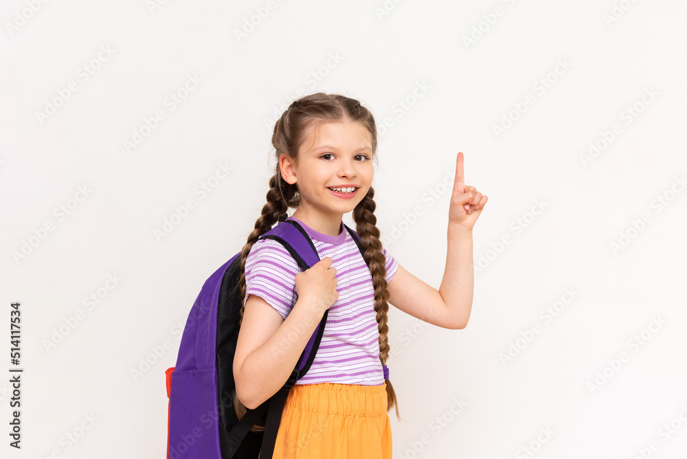 A child with a school backpack points up at your advertisement on a white isolated background. A little girl with pigtails points to the announcement of courses for children. A child with a school backpack points up at your advertisement on a white isolated background. A little girl with pigtails points to the announcement of courses for children.
