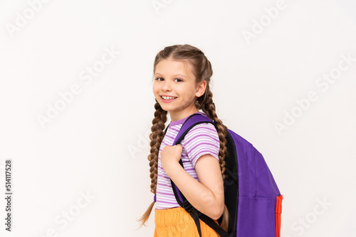 A little girl with a backpack on her back in orange shorts on a white isolated background. Summer educational courses for children.