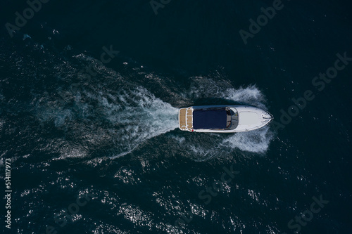 A white big boat with a blue awning is moving fast on dark water. Aerial view. Big white boat with an awning moving on the water top view. © Berg