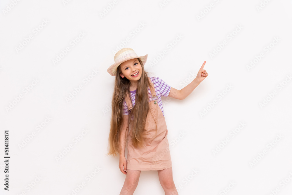 A beautiful little girl in a summer sundress and a straw hat on a white isolated background points her index finger up at your advertisement. A beautiful little girl in a summer sundress and a straw hat on a white isolated background points her index finger up at your advertisement.