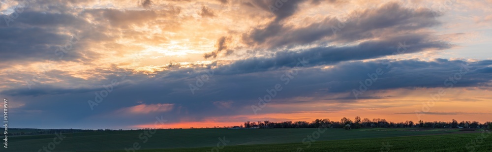 Sun sitting on the horizon against the background of colorful clouds in the sky 