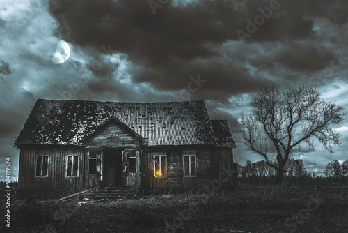 Old wooden house,dramatic clouds at night. Abandoned Haunted Horror House.Near is one tree at night with a moon.