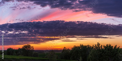 Sun sitting on the horizon against the background of colorful clouds in the sky 