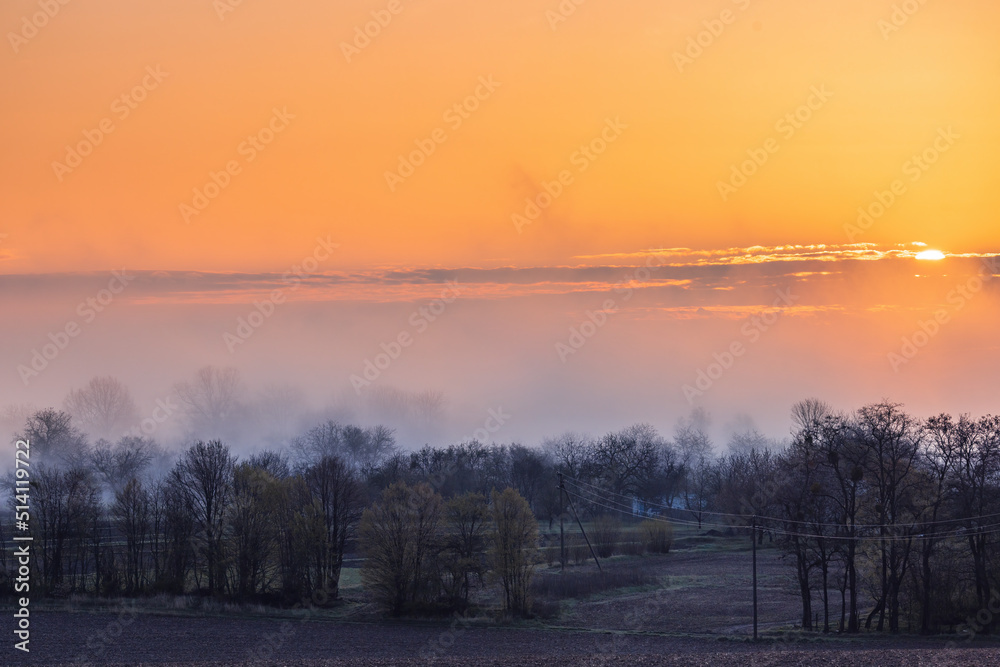 Colorful sunrise over trees, fields and village in spring in Ukraine