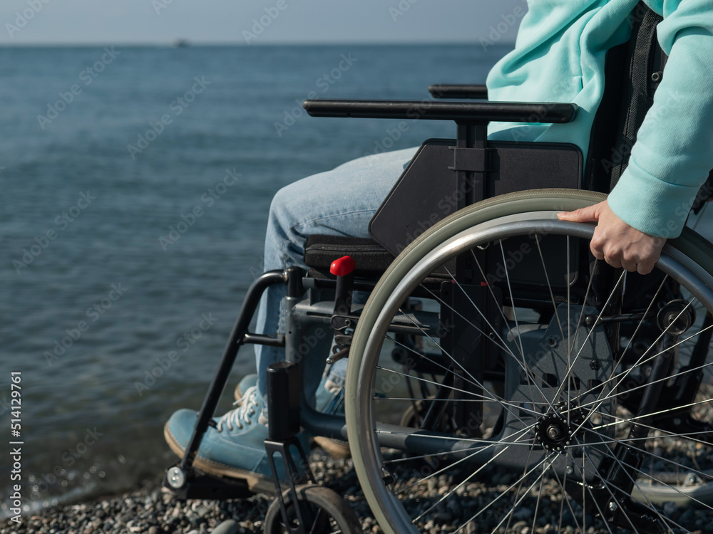Obraz premium Caucasian woman in a wheelchair on the seashore. Close-up of female hands.