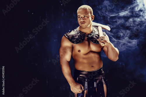 Studio shot of muscular ancient warrior man posing with axe