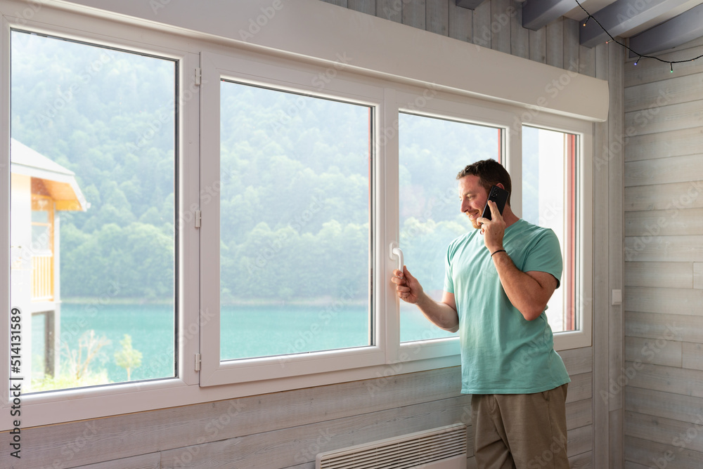 Fototapeta premium Smiled man talking by phone leaning on the window of his apartment.